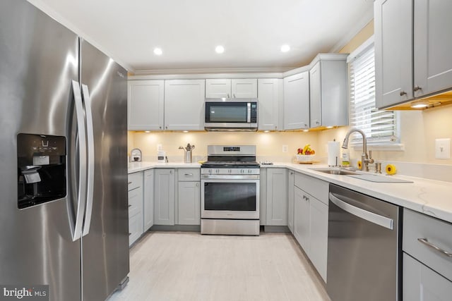 kitchen with appliances with stainless steel finishes, gray cabinets, a sink, and light wood-style floors