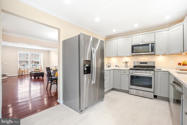 kitchen featuring gray cabinetry, stainless steel appliances, light countertops, ornamental molding, and light wood-type flooring