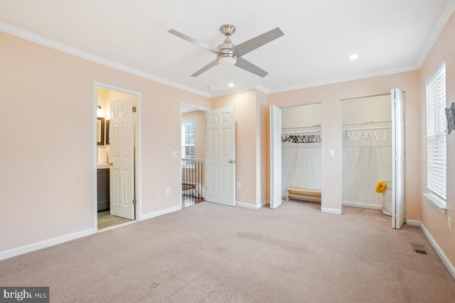 unfurnished bedroom featuring crown molding, baseboards, two closets, and light colored carpet