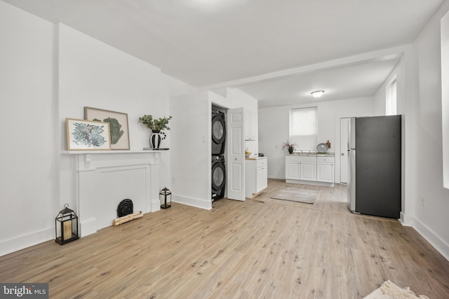 unfurnished living room with light wood-type flooring, stacked washing maching and dryer, and baseboards