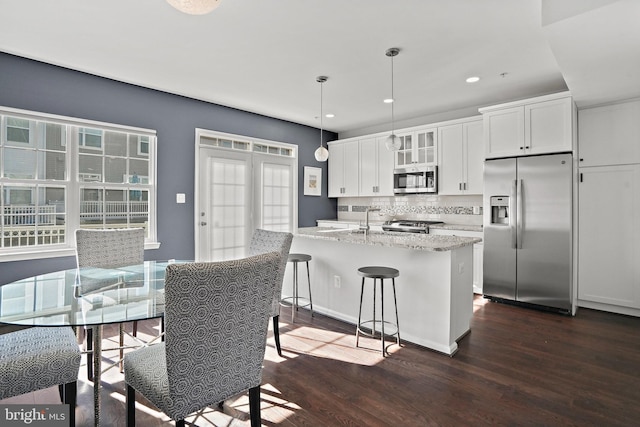 kitchen with appliances with stainless steel finishes, white cabinetry, an island with sink, dark hardwood / wood-style flooring, and decorative light fixtures