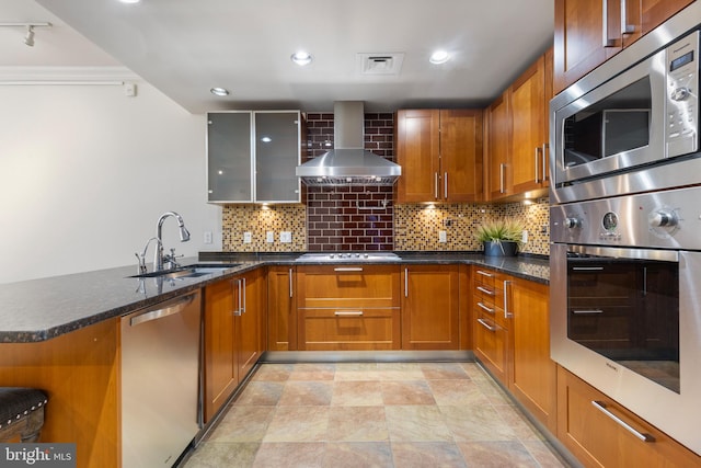 kitchen featuring appliances with stainless steel finishes, tasteful backsplash, kitchen peninsula, dark stone counters, and wall chimney exhaust hood