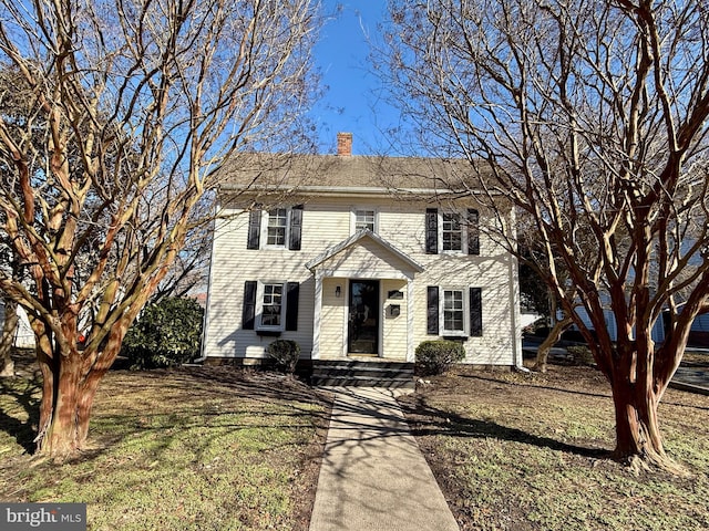 colonial-style house with a chimney and a front lawn