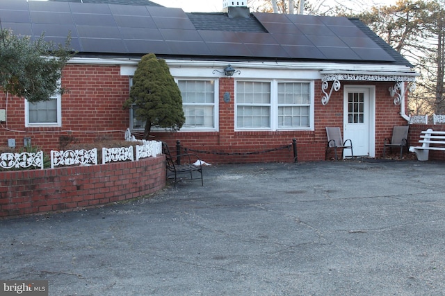 exterior space with brick siding, roof with shingles, and solar panels