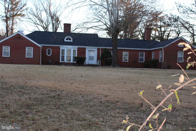 single story home featuring brick siding, a chimney, and a front yard