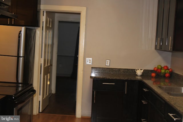 kitchen with dark wood-style floors, electric range, freestanding refrigerator, a sink, and dark stone counters