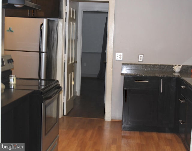 kitchen with stainless steel appliances, dark countertops, wall chimney range hood, and wood finished floors