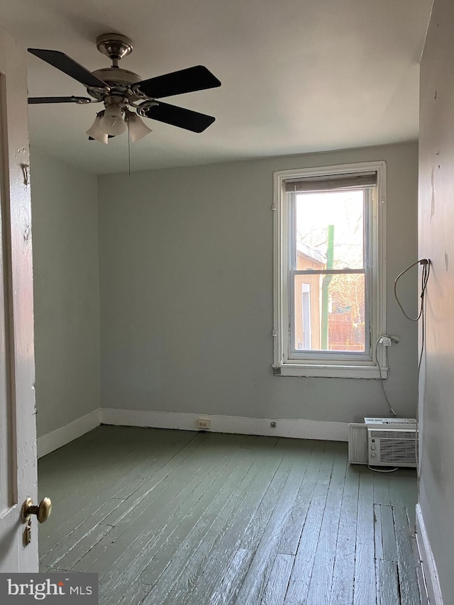 empty room featuring a ceiling fan, a wall unit AC, baseboards, and wood finished floors