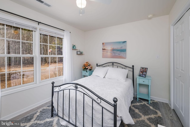 bedroom with baseboards, visible vents, a ceiling fan, wood finished floors, and a closet