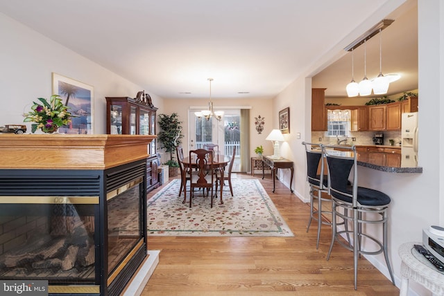 dining room featuring light wood finished floors, baseboards, a chandelier, and a multi sided fireplace