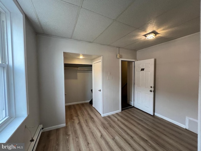 unfurnished bedroom featuring wood-type flooring, a drop ceiling, a closet, and a baseboard heating unit