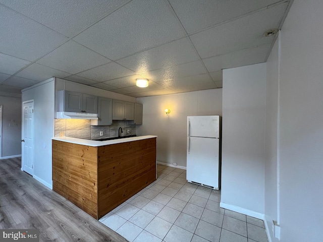 kitchen featuring a paneled ceiling, gray cabinetry, backsplash, white fridge, and light tile patterned floors