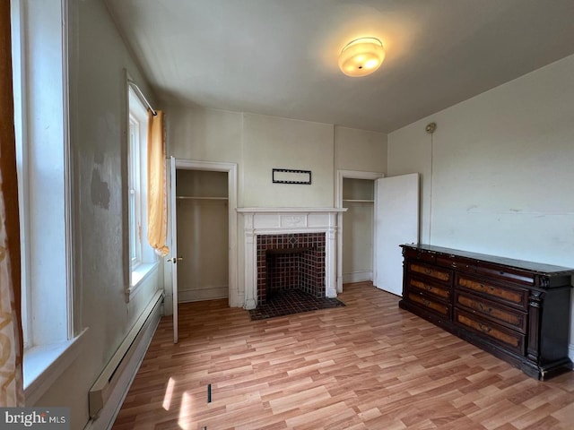 interior space with a tiled fireplace, a baseboard heating unit, and light hardwood / wood-style floors