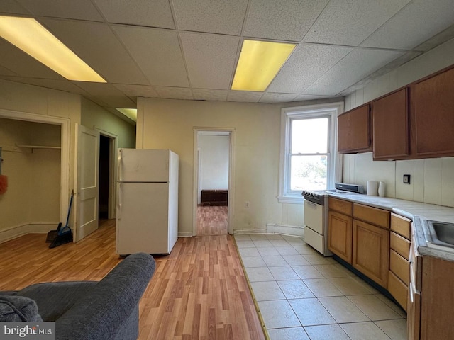 kitchen with white appliances, tile countertops, a paneled ceiling, and light hardwood / wood-style flooring