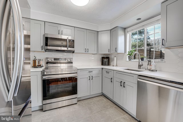 kitchen featuring appliances with stainless steel finishes, sink, gray cabinetry, a textured ceiling, and decorative backsplash