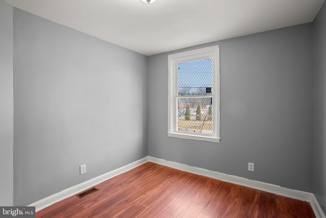 spare room featuring wood finished floors, visible vents, and baseboards