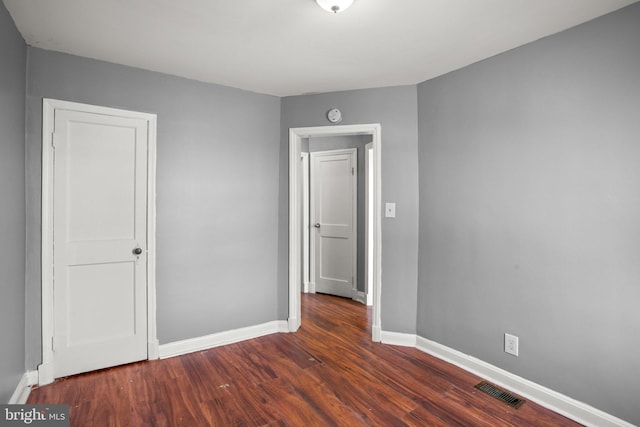 unfurnished room with dark wood-style flooring, visible vents, and baseboards