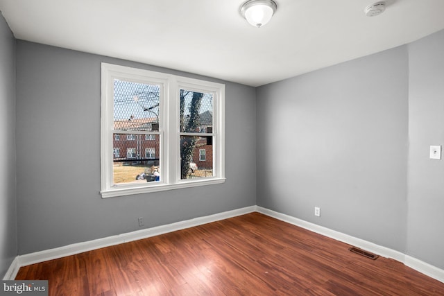 empty room with dark wood-type flooring, visible vents, and baseboards