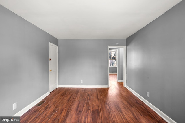 unfurnished room with dark wood-style floors, visible vents, and baseboards