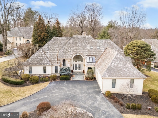 french provincial home featuring driveway, stone siding, stucco siding, a chimney, and a front yard