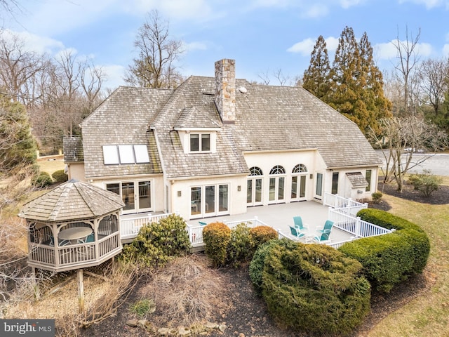 rear view of house featuring french doors, a chimney, stucco siding, a gazebo, and fence