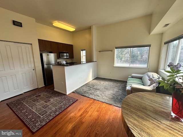 kitchen featuring lofted ceiling, stainless steel appliances, kitchen peninsula, hardwood / wood-style flooring, and dark brown cabinetry