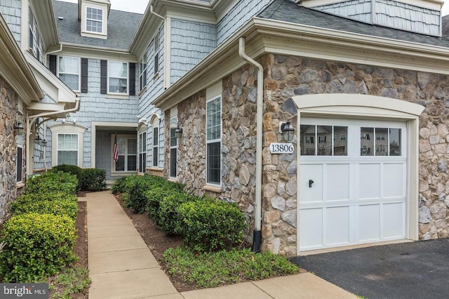 property entrance featuring a shingled roof, stone siding, and a garage