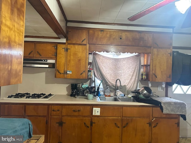 kitchen with under cabinet range hood, a sink, white gas cooktop, light countertops, and brown cabinetry