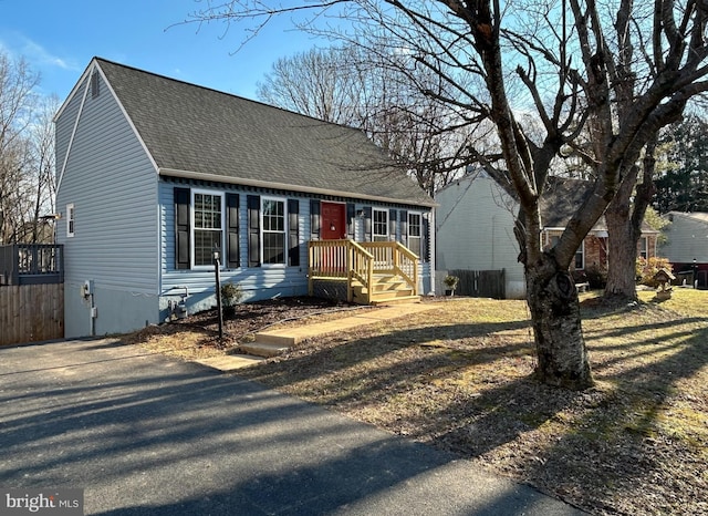 cape cod-style house featuring fence and roof with shingles