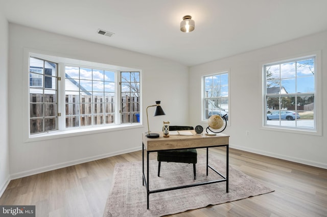 office space with light wood-type flooring, visible vents, and baseboards