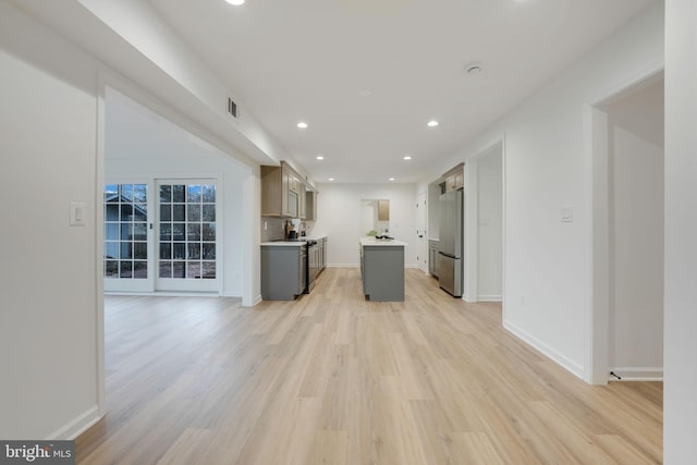 kitchen featuring visible vents, freestanding refrigerator, a center island, light countertops, and light wood-style floors