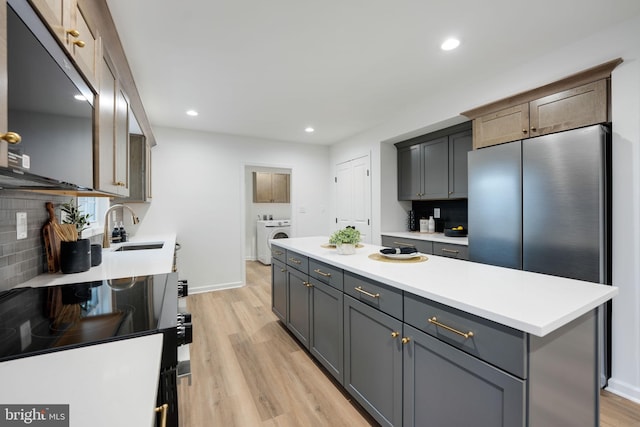 kitchen with a kitchen island, a sink, light countertops, decorative backsplash, and washer / clothes dryer