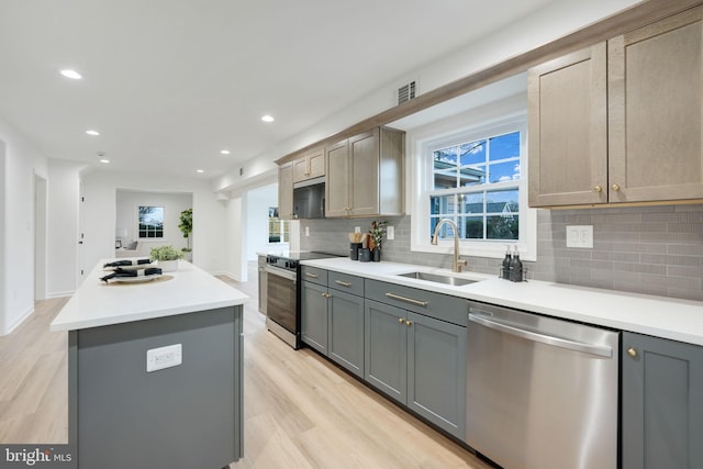 kitchen featuring a kitchen island, stainless steel appliances, light countertops, gray cabinetry, and a sink