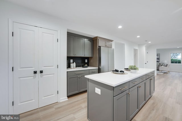 kitchen featuring a kitchen island, freestanding refrigerator, gray cabinets, light countertops, and light wood-style floors