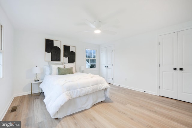 bedroom with baseboards, visible vents, two closets, and light wood finished floors