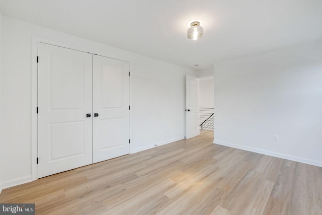 unfurnished bedroom featuring light wood-style floors, baseboards, and a closet