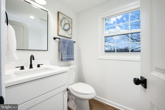 half bath with wood finished floors, vanity, toilet, and baseboards