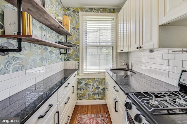 kitchen featuring dark wood-type flooring, stainless steel gas range, sink, dark stone countertops, and white cabinets