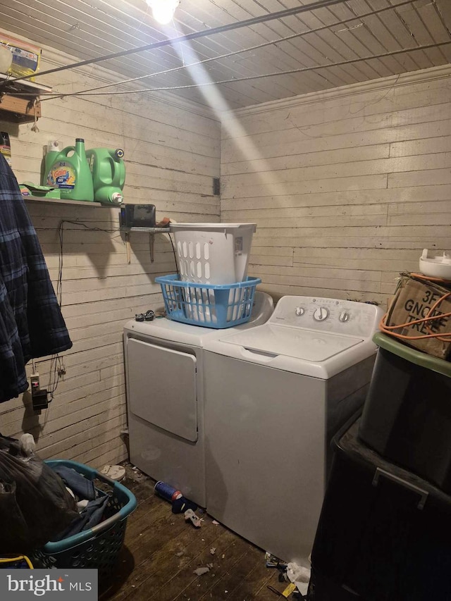 clothes washing area with wood-type flooring, washer and dryer, and wood walls