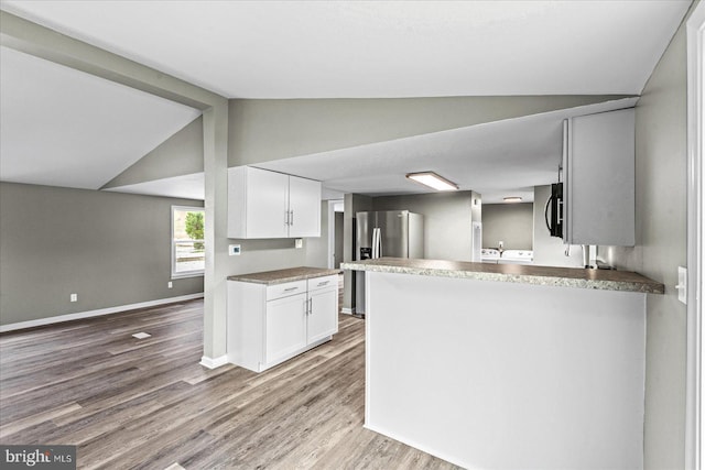 kitchen featuring white cabinetry, stainless steel fridge, kitchen peninsula, and vaulted ceiling