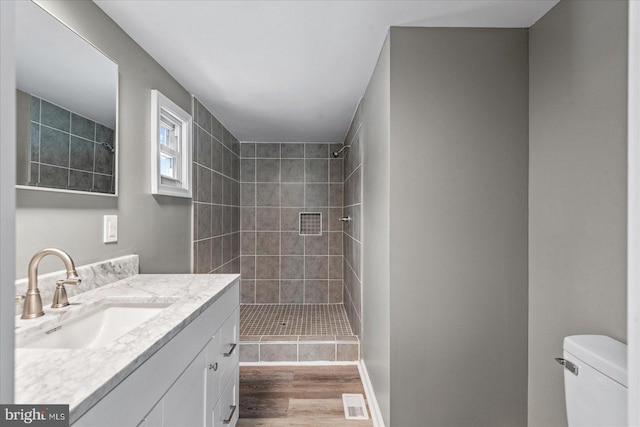 bathroom with hardwood / wood-style flooring, tiled shower, vanity, and toilet