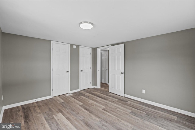 unfurnished bedroom with multiple closets and light wood-type flooring