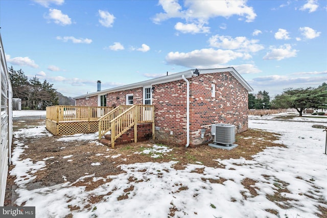 snow covered property with central air condition unit and a deck