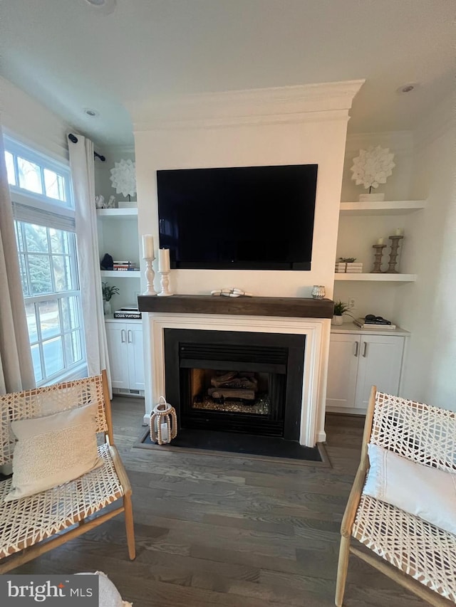 living area featuring a fireplace with flush hearth, built in shelves, ornamental molding, and dark wood-style flooring