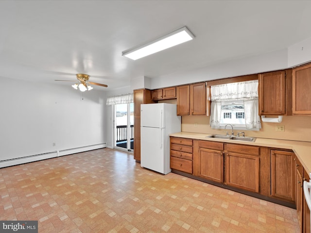 kitchen with brown cabinetry, ceiling fan, freestanding refrigerator, light countertops, and a sink