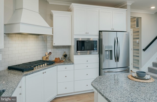 kitchen with stainless steel appliances, white cabinetry, custom range hood, and ornamental molding