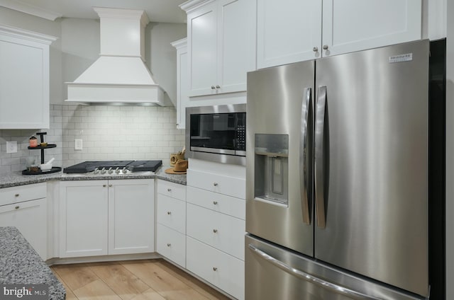 kitchen featuring light stone counters, tasteful backsplash, appliances with stainless steel finishes, custom range hood, and white cabinets