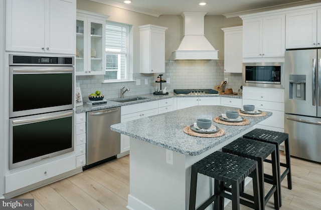 kitchen with white cabinetry, sink, custom exhaust hood, light stone counters, and stainless steel appliances