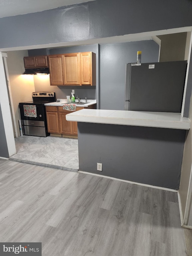 kitchen featuring light wood finished floors, light countertops, appliances with stainless steel finishes, under cabinet range hood, and brown cabinets