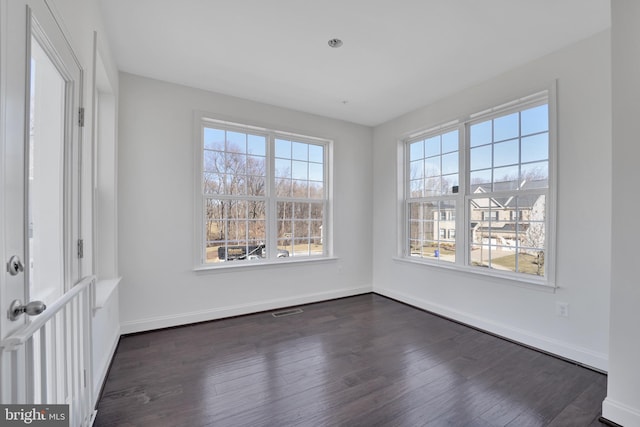 spare room featuring visible vents, baseboards, and dark wood finished floors